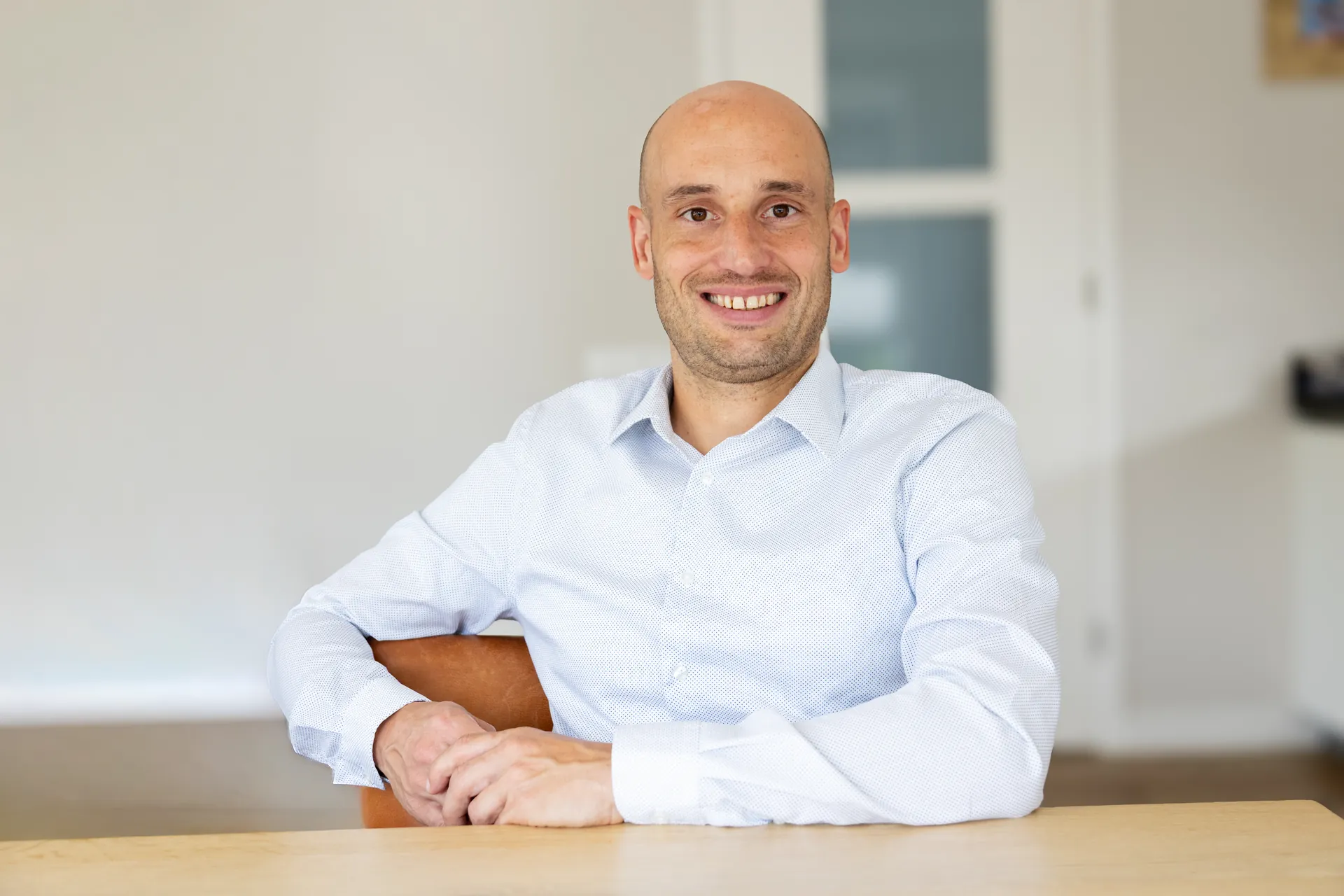 Thijs Logtenberg zit lachend aan tafel, in een wit overhemd.