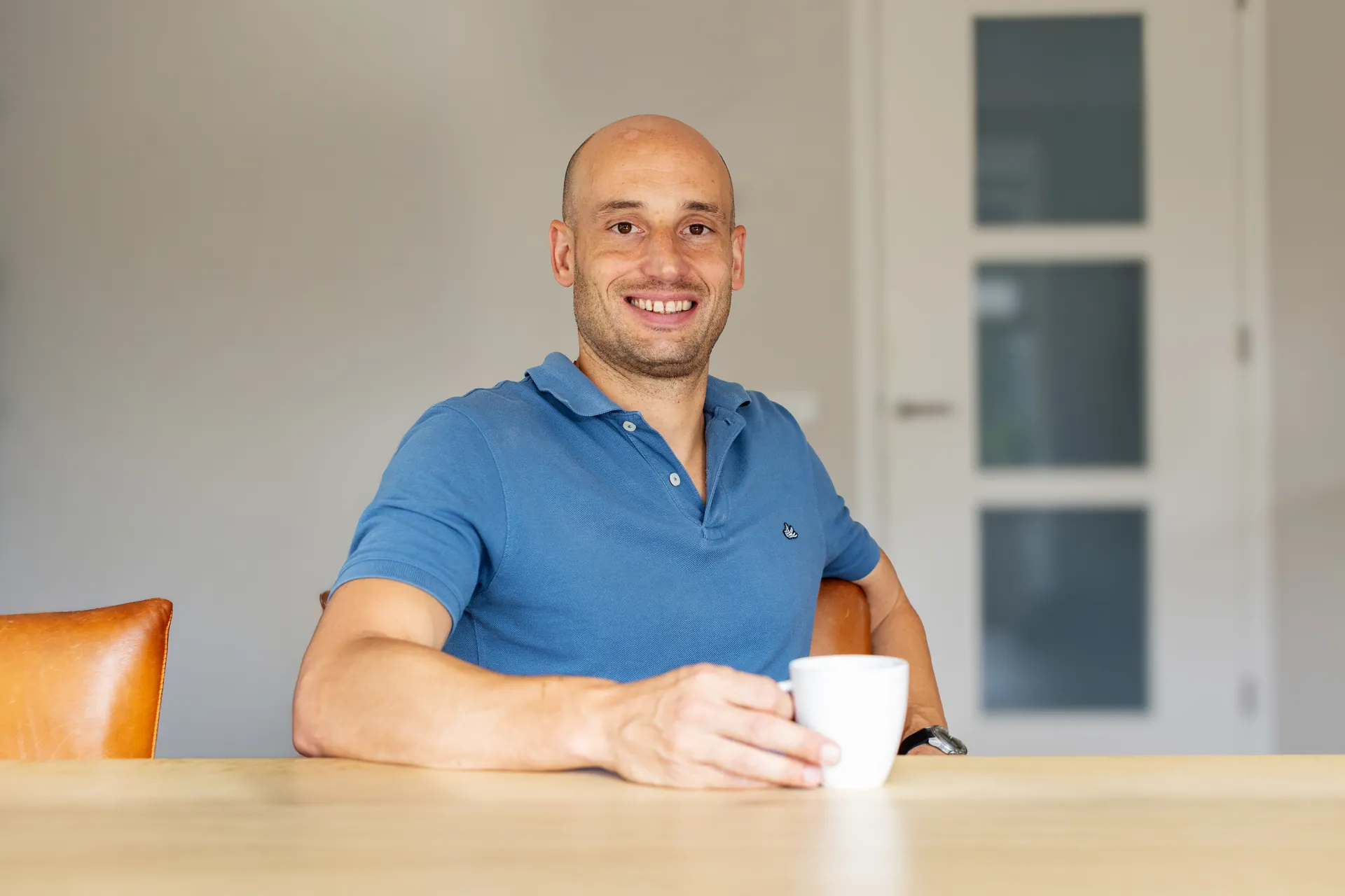 Thijs Logtenberg lachend aan tafel met een kop koffie.